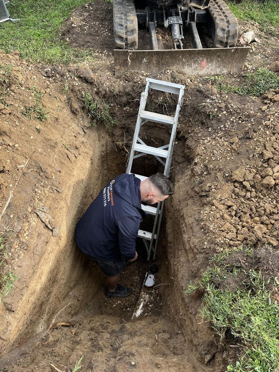 Plumber inspecting an excavated drainage line, Malvern